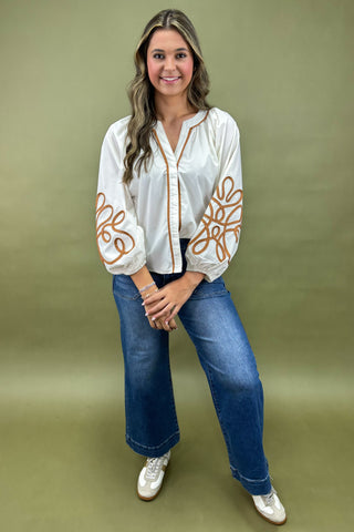 Woman wearing a white blouse with brown patterns and blue jeans on a green background