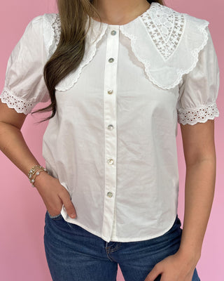White blouse with lace details worn by a person on a pink background