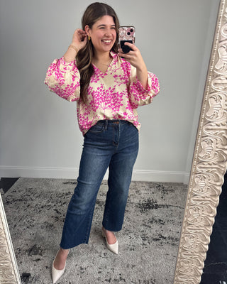 Woman taking a mirror selfie wearing a floral blouse and jeans.