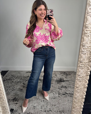 Woman taking a mirror selfie wearing a pink floral blouse and blue jeans.