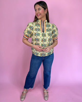 Woman wearing a patterned blouse and jeans against a pink background