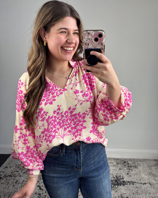 Woman taking a mirror selfie wearing a pink floral blouse and blue jeans.