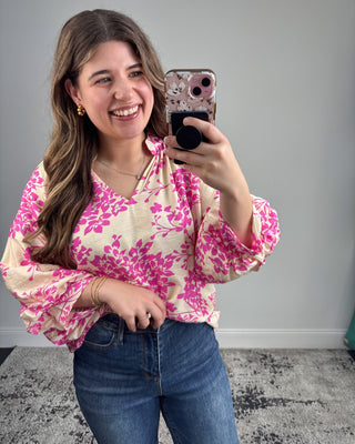 Woman taking a mirror selfie wearing a pink floral blouse and blue jeans.