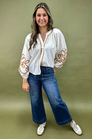 Woman wearing a white blouse with floral embroidery and blue jeans on a green background