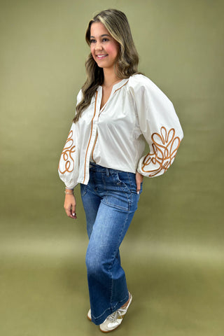 Woman wearing a white blouse with floral designs and blue jeans on a green background