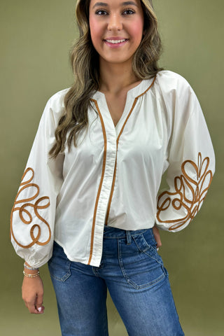 Woman wearing a white blouse with brown embroidery and blue jeans against a green background