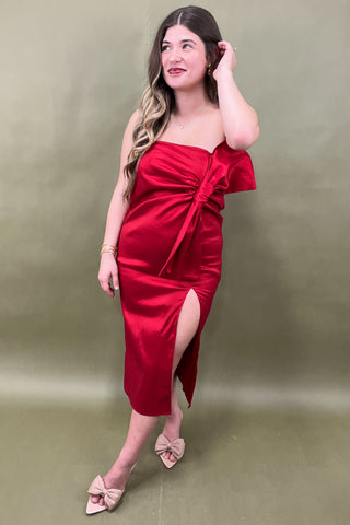 Woman wearing a red strapless dress with a slit on a plain background