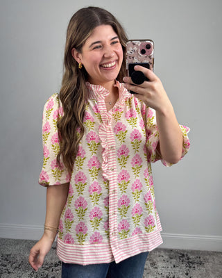 Woman taking a selfie wearing a floral blouse against a gray background