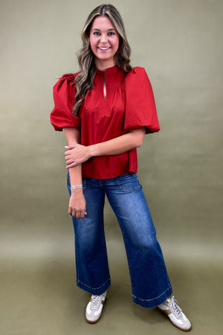 Woman wearing a red blouse and blue jeans against a green background