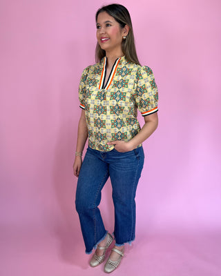 Woman wearing a patterned blouse and jeans against a pink background