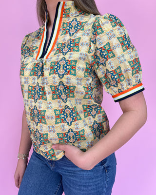 Person wearing a colorful patterned shirt with blue jeans against a pink background
