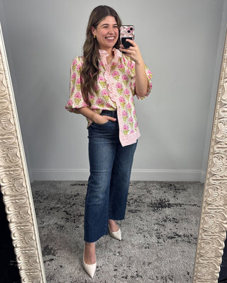 Woman taking a mirror selfie wearing a floral blouse and jeans.