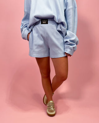 Person wearing a light blue outfit with shorts on a pink background