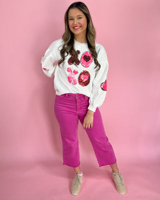 Woman wearing a white sweatshirt with pink sequin designs and pink pants on a pink background