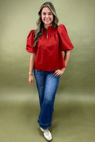 Woman wearing a red blouse with puff sleeves and blue jeans on a green background