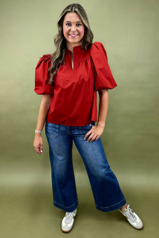 Woman wearing a red blouse and blue jeans against a green background