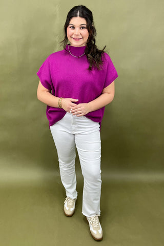 Person wearing a purple top and white pants against a green background