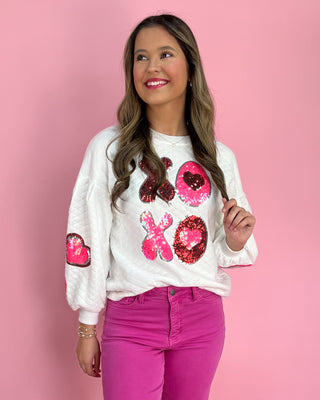 Woman wearing a white sweatshirt with pink sequin designs on a pink background