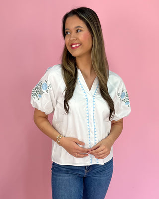 Woman wearing a white blouse with floral embroidery on a pink background