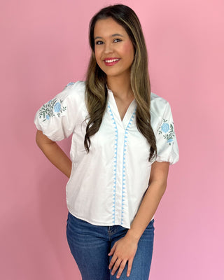 Woman wearing a white blouse with floral embroidery against a pink background