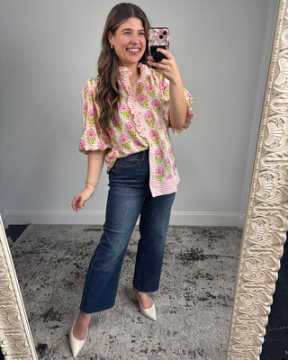Woman taking a mirror selfie wearing a floral blouse and jeans.