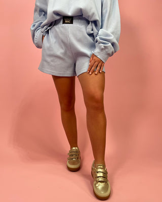 Person wearing a light gray sweatshirt and shorts with gold sneakers on a pink background