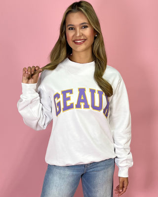 Woman wearing a white sweatshirt with 'GEAU' printed in purple and yellow on a pink background