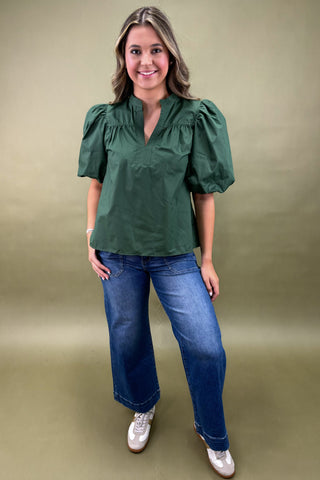 Woman wearing a green blouse and blue jeans against a beige background