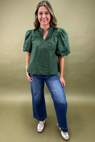 Woman wearing a green blouse and blue jeans against a green background