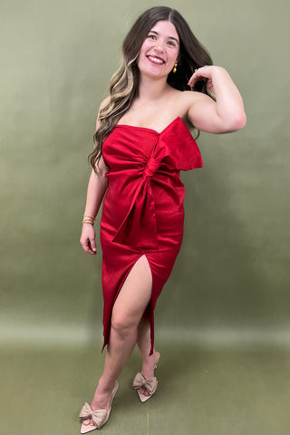 Woman wearing a red strapless dress with a slit on a green background