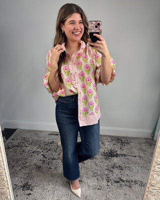Woman taking a mirror selfie wearing a floral blouse and jeans.