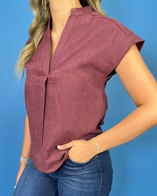 Burgundy cap sleeve blouse with a split V-neckline, subtle textured finish, and relaxed fit.