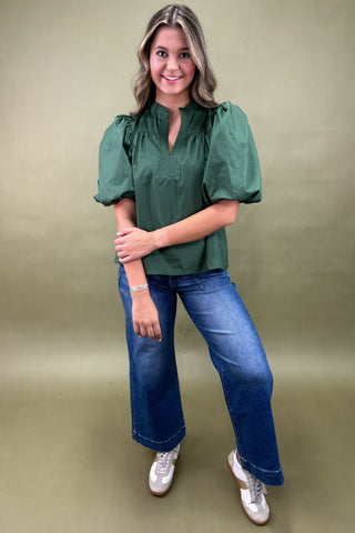 Woman wearing a green blouse and blue jeans against a beige background