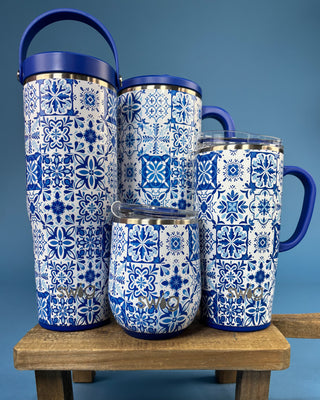 Four blue and white patterned insulated tumblers with blue lids and handles, arranged on a wooden stool against a blue background.