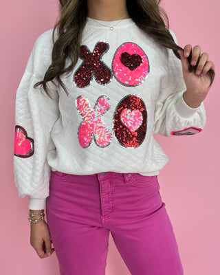 Person wearing a white sweatshirt with sequin designs on a pink background
