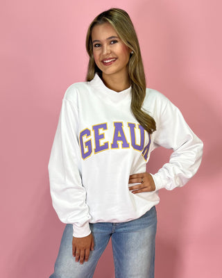 Woman wearing a white sweatshirt with 'GEAUA' printed on it against a pink background