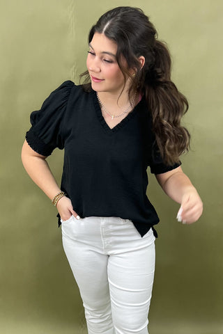 Woman wearing a black top and white pants against a green background