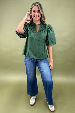 Woman wearing a green blouse and blue jeans against a green background