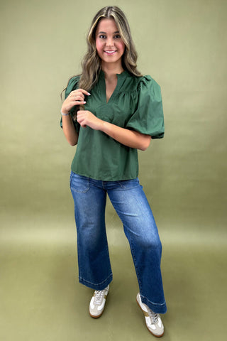 Woman wearing a green blouse and blue jeans against a green background