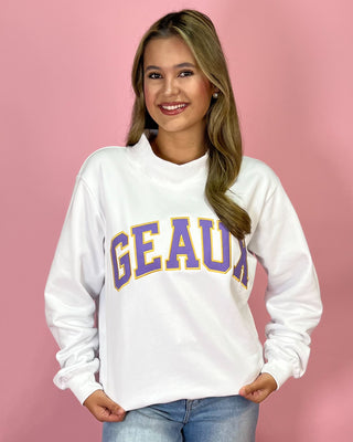 Person wearing a white sweatshirt with 'GEAUX' printed in purple and yellow on a pink background