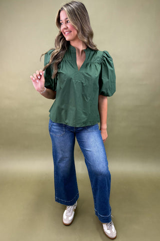Woman wearing a green blouse and blue jeans against a beige background