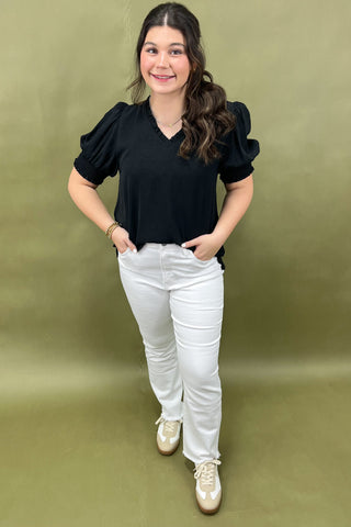 Woman wearing a black top and white pants against a green background