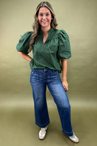 Woman wearing a green blouse and blue jeans against a beige background