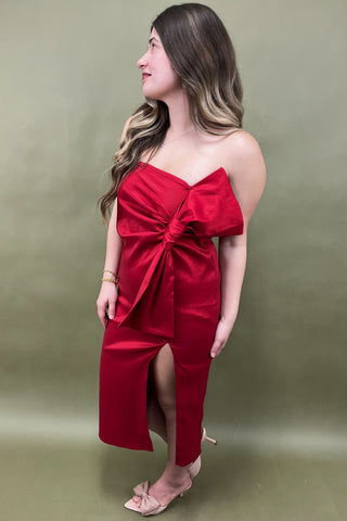 Woman wearing a red off-shoulder jumpsuit with a bow detail on a green background