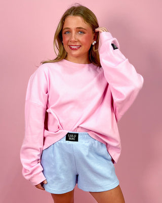 Person wearing a pink sweatshirt and light blue shorts against a pink background