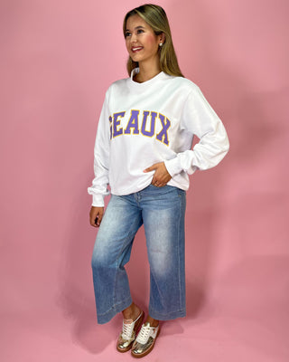Woman wearing a white sweatshirt with 'BEAUX' text and blue jeans on a pink background