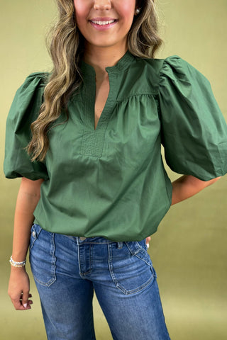 Woman wearing a green blouse with puffed sleeves and blue jeans on a yellow background