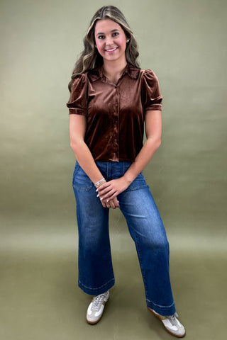 Woman wearing a brown satin blouse and blue jeans against a green background