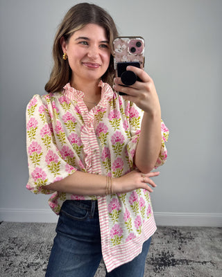 Woman taking a mirror selfie wearing a floral blouse and jeans on a gray background