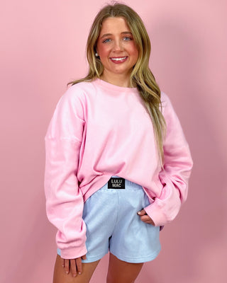 Person wearing a pink sweatshirt with a visible brand logo on a pink background